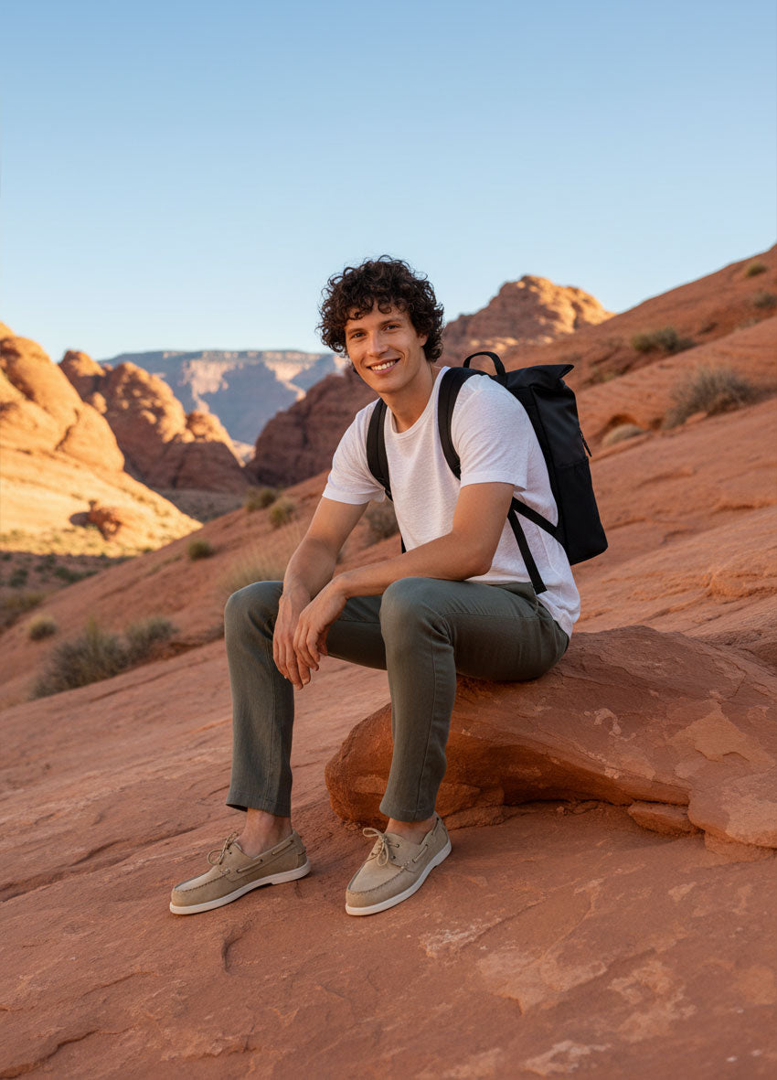 VIVID – Herr mit schwarzem Rucksack in weißem T-Shirt und Olive Chino sitzend auf Sandsteinfelsen im Canyon