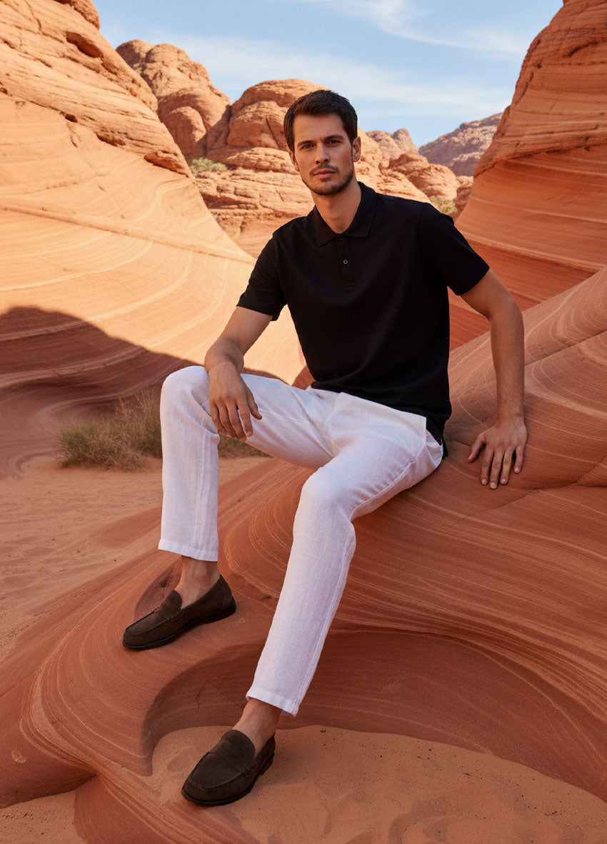 VIVID – Herr in schwarzem Polo-Shirt und weißer Hose sitzend auf Sandsteinfelsen im Canyon